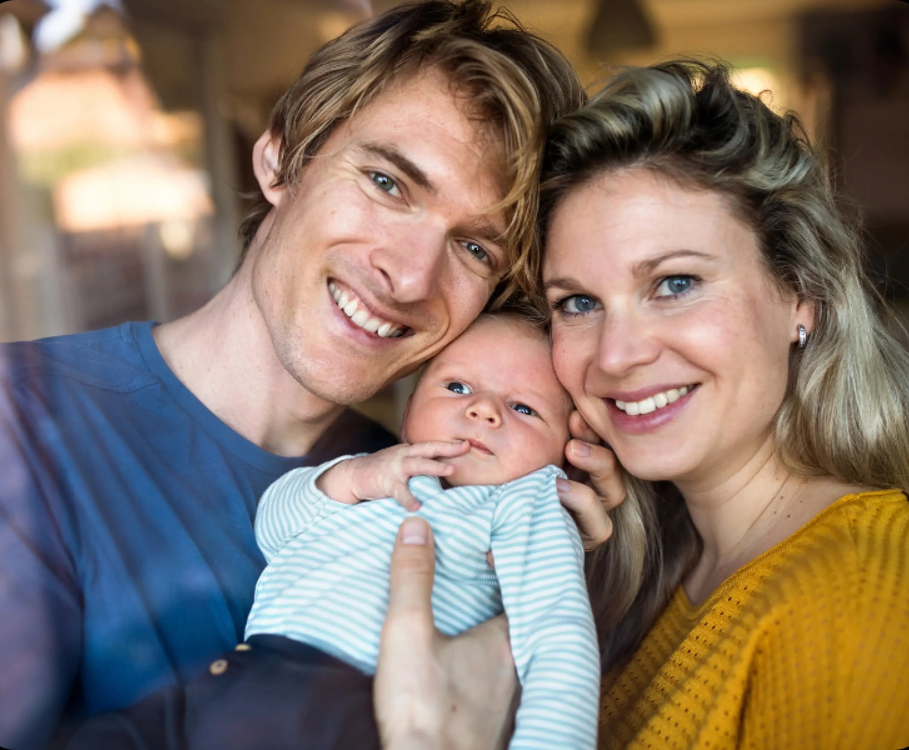 Jonge ouders met baby kijken stralend in de camera en groeien in het ouderschap